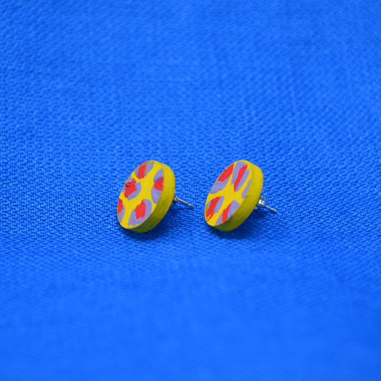 A pair of round yellow earrings with a red and muted purple abstract leopard print pattern, displayed on a textured blue fabric background.