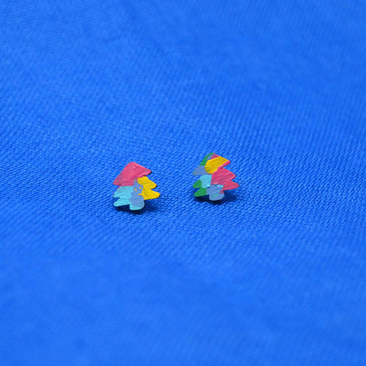 A pair of small multicolor stud earrings shaped like stylized trees, resting on a textured blue background.