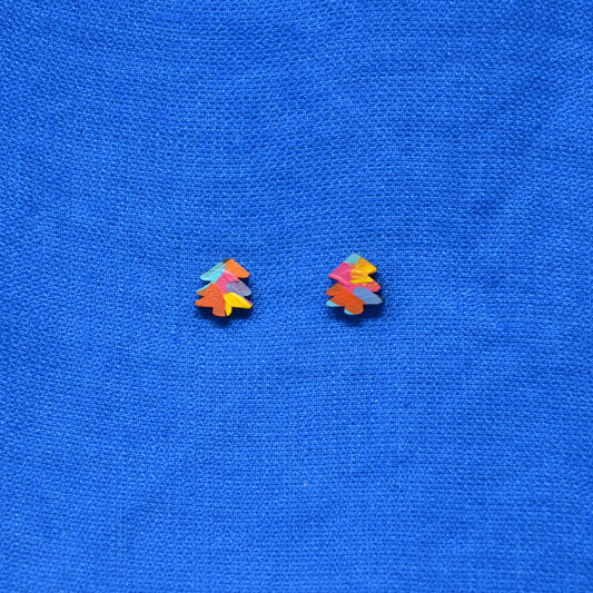 A pair of small multicolor tree stud earrings with layered paimt in orange, pink, yellow, blue, and purple, displayed on a textured blue background.