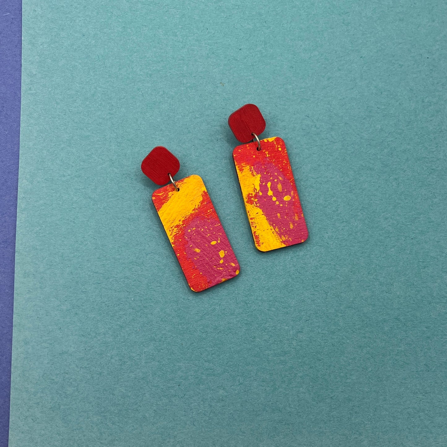 Colorful rectangular earrings on a teal background