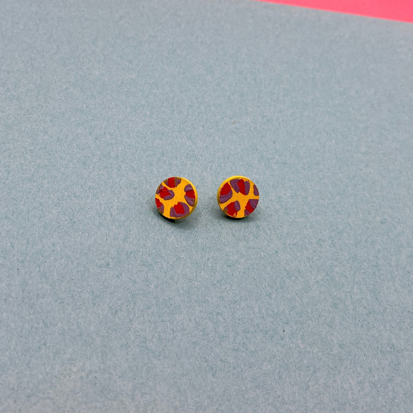 Round earrings with a red, purple and yellow pattern on a blue background