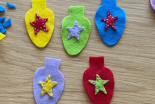 Colorful felt Christmas light bulb ornaments with star decorations on a wooden surface.
