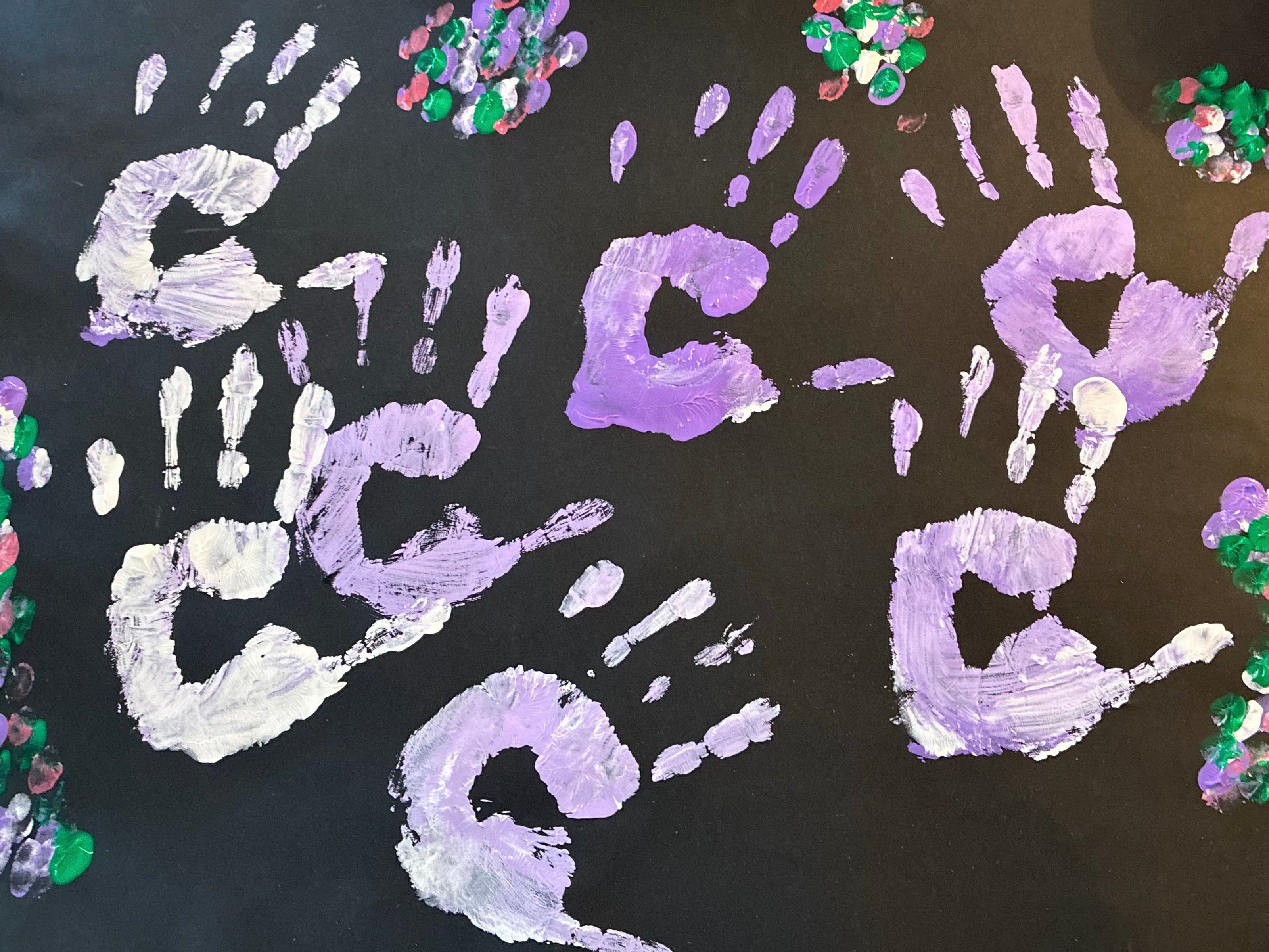 Black paper featuring painted purple and white handprints