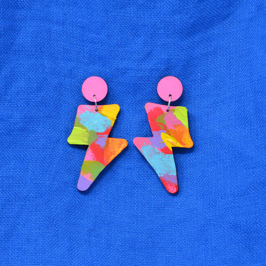 A pair of wooden lightning shaped stud dangle earrings.  With light pink circle stud top and hanging bolt painted in bright colours.