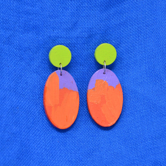 A pair of handmade drop earrings with bright lime green circular studs and oval dangles featuring a split orange and purple design, displayed on a textured blue background.