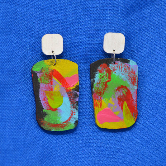 A pair of colorful rectangular drop earrings with white rounded square posts, featuring an abstract marbled pattern in pink, green, yellow, and blue on a textured blue background.