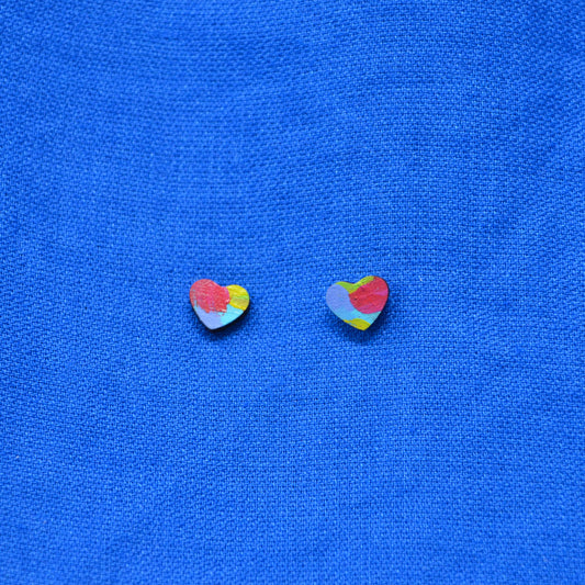 Two small heart-shaped stud earrings with a multicolor abstract paint-stroke pattern, displayed on a textured blue fabric background.