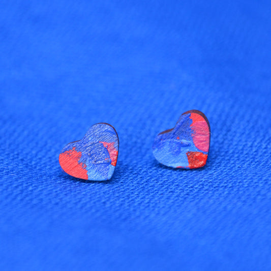 A pair of small heart-shaped earrings with a painted blue and red pattern, displayed on a textured blue background.