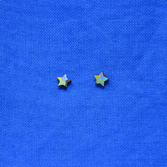 Two small star-shaped stud earrings with a black, yellow, green, purple and blue painted pattern, displayed on a textured blue background.