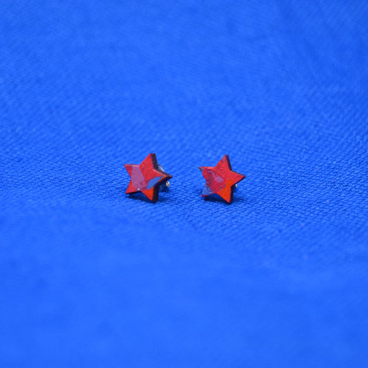 A pair of small red star-shaped stud earrings on a textured bright blue background.