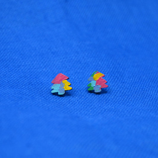 A pair of small multicolor stud earrings shaped like stylized trees, featuring pink, yellow, green and light blue abstract painting, placed on a textured blue fabric background.