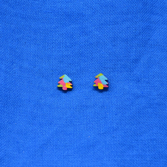 A pair of small multicolor stud earrings shaped like stylized Christmas trees, placed on a textured blue fabric background.