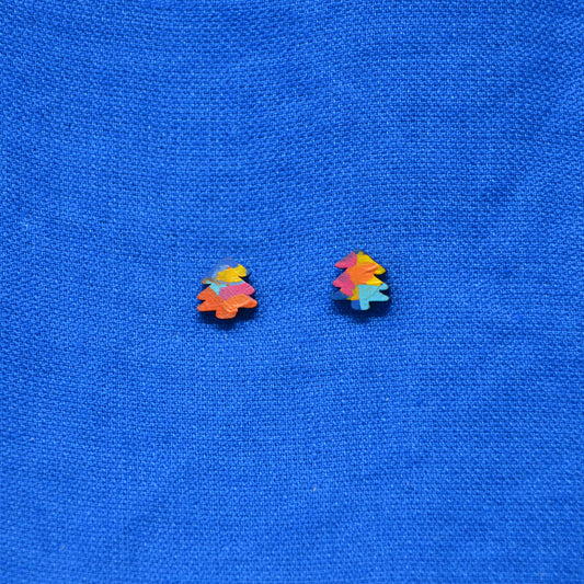 A pair of small multicolor Christmas tree stud earrings on a textured blue fabric background.