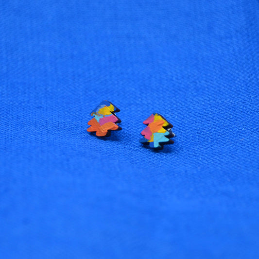 A pair of small multicolor tree stud earrings with layered paint in orange, pink, yellow and blue, displayed on a textured blue background.