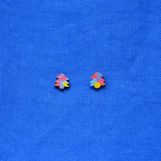A pair of small multicolor stud earrings shaped like stylized Christmas trees, placed on a textured blue fabric background.
