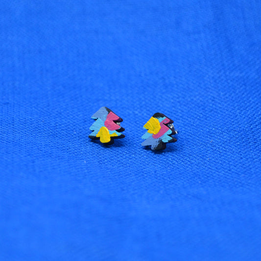 A pair of small multicolor tree stud earrings with layered paint in black, pink, yellow and blue, displayed on a textured blue background.