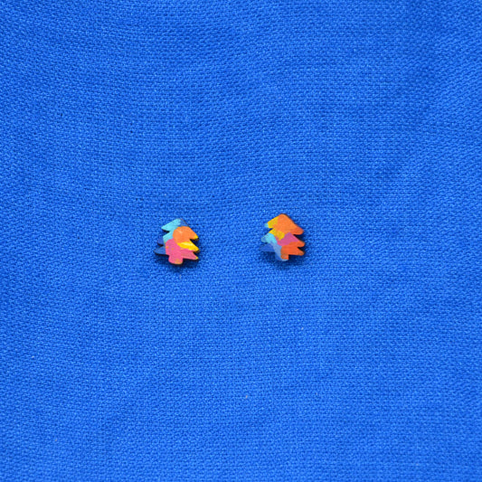 A pair of small multicolor Christmas tree stud earrings on a textured blue fabric background.