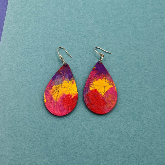 Colorful teardrop earrings on a two-tone purple and blue background