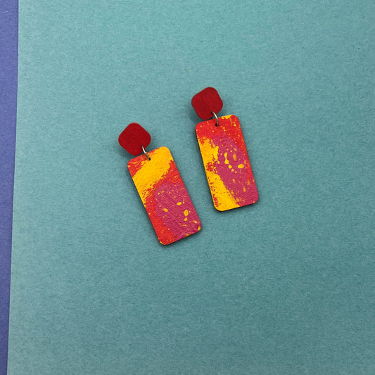 Colorful rectangular earrings on a teal background