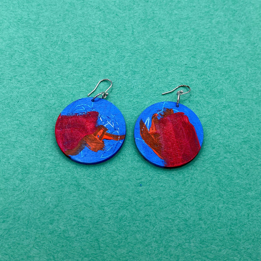 Pair of round earrings with red and blue design on a green background
