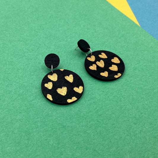 Black earrings with gold heart patterns on a green and blue geometric background