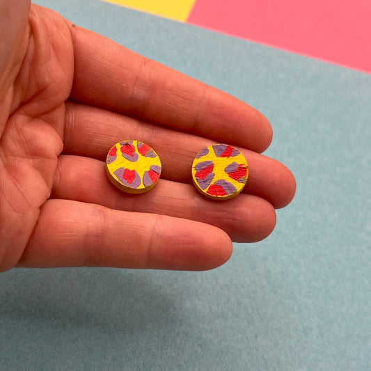 Colorful circular earrings held between fingers against a multicolored background