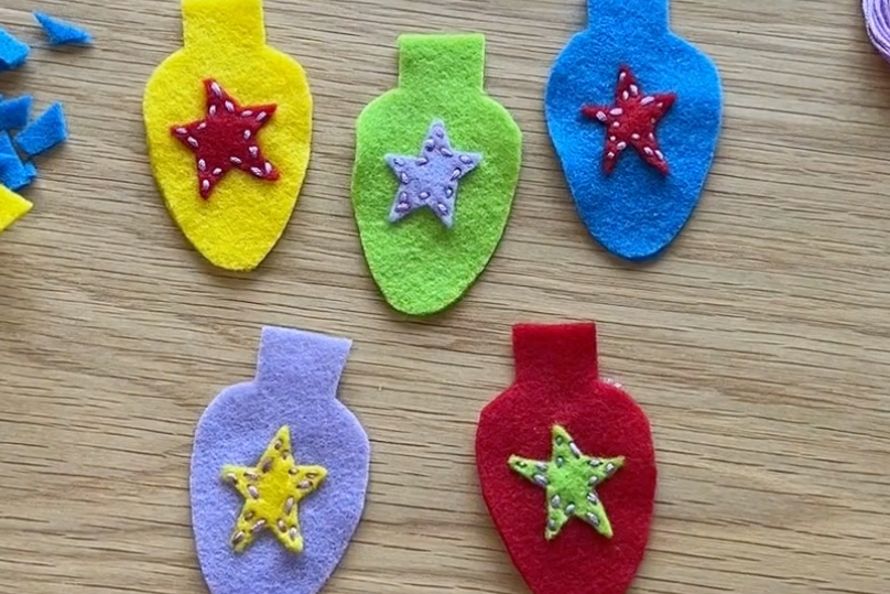 Colorful felt Christmas light bulb ornaments with star decorations on a wooden surface.